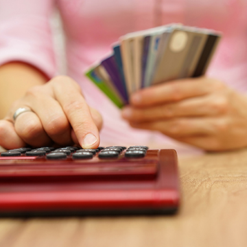 CreditCardScore.jpg Person typing on calculator while holding stack of credit cards